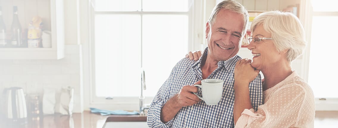 Uśmiechnięta para senior&oacute;w pijąca kawę w kuchni